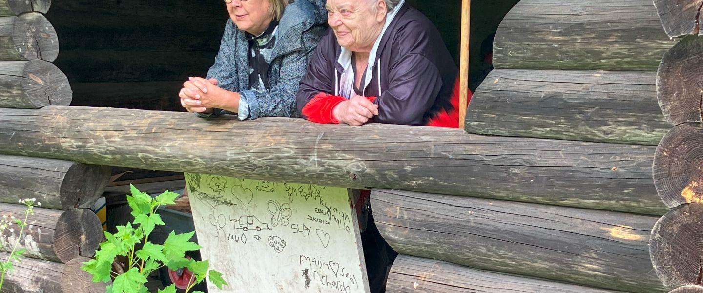 Kaksi hyväntuulista naista kurkistaa grillikodan aukosta