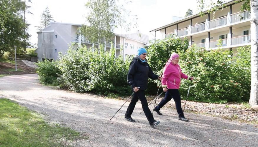 Naiset sauvakävelyllä, takana majoitusrakennuksia