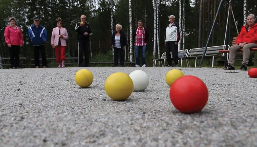 Lähikuvassa boccia-pallot ja taustalla eläkeläisiä pelaamassa