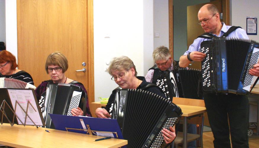 Neljä harmonikansoittajaa keskittyy tiiviisti, opettaja Seppo Lankisen soittaessa vieressä.
