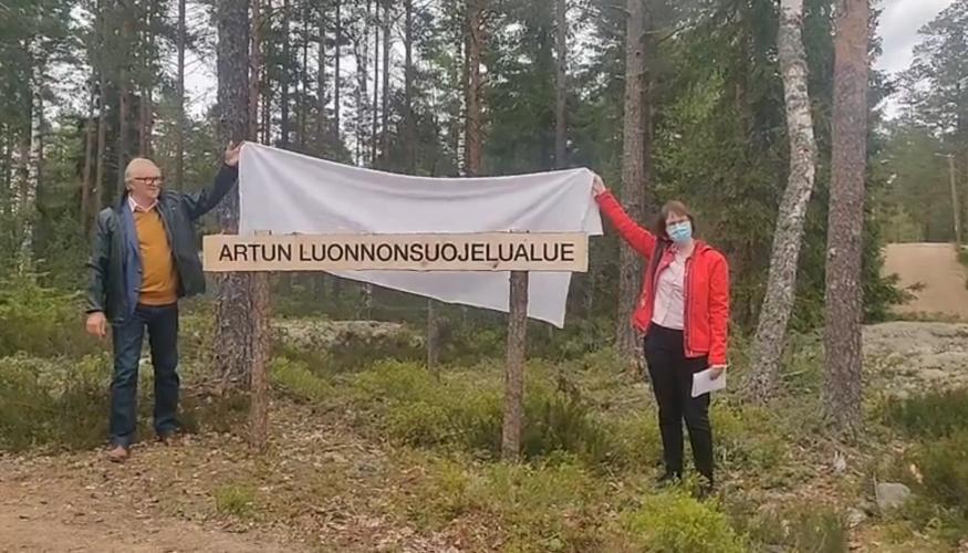 Eläkeliiton puheenjohtaja Raimo Ikonen ja Lehmirannan lomakeskuksen johtaja Tanja Bergroth nostavat lakanan pois luonnonsuojelualueen kyltin päältä metsän reunassa Salossa.